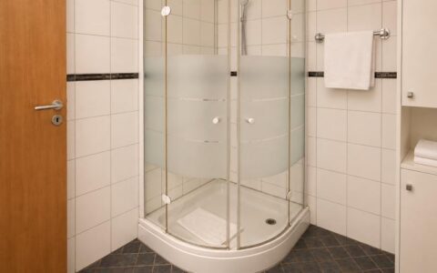 Modern Verdo Hotel deluxe bathroom with glass corner shower, clean white tiles, and bright boutique hotel interior.