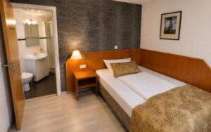 Verdo Hotel deluxe room with comfortable single bed, warm bedside lighting, modern bathroom entrance, and cozy boutique interior.